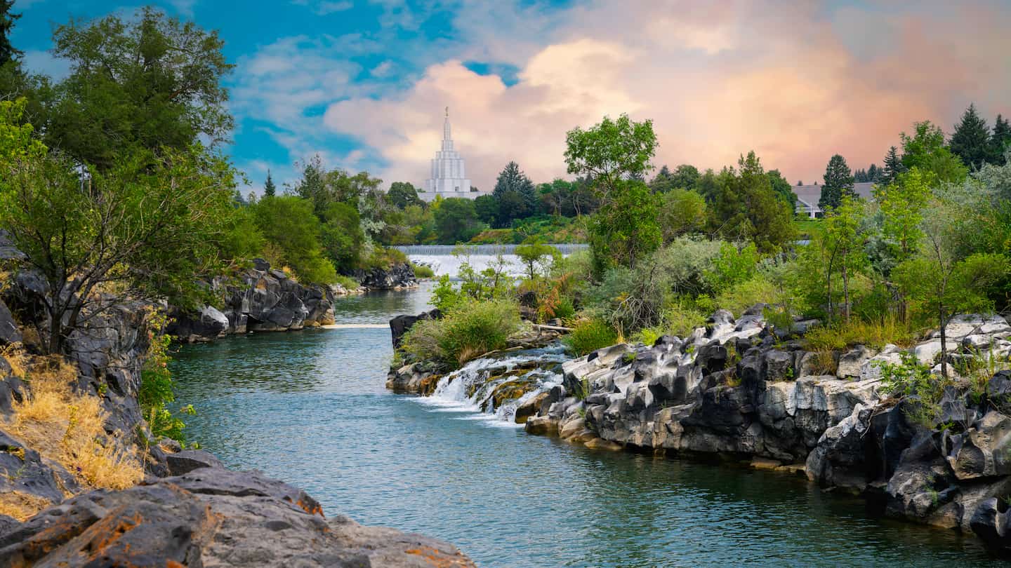 A river flows through a rocky landscape, surrounded by trees and boulders in Idaho Falls, ID.